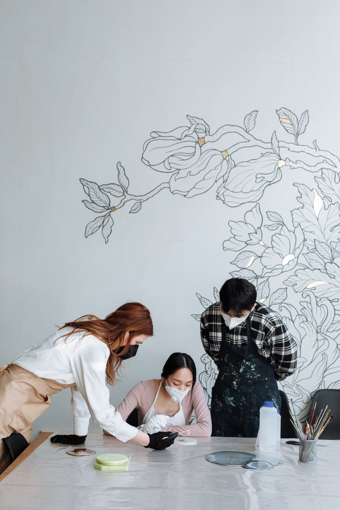 Three people working together on an art project, wearing masks for safety.